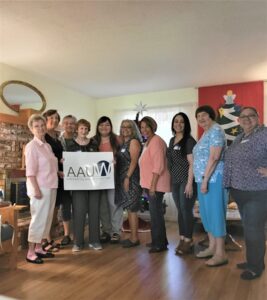 Past presidents of AAUW Porterville branch and some current members stand in a group with the AAUW sign in front of them. They are joined to celebrate an anniversary of the organization.